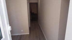 Un couloir avec un plancher en bois, des murs blancs et une porte sur le côté gauche.