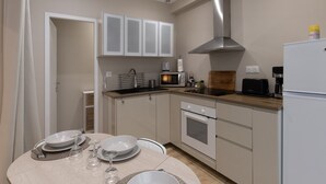A kitchen with white cabinets, a microwave, a stove, and a refrigerator. - Appart 100 - Cosy T2 with TV (Bourg-Saint-Andéol)