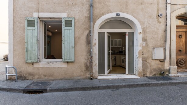 A building with a ground-floor entrance, a visible kitchen area, and a number '13' on the wall. - Appart 100 - Cosy T2 with TV (Bourg-Saint-Andéol)