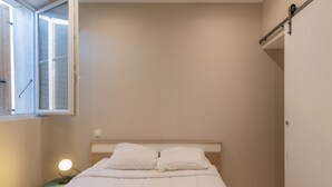 A bedroom with a bed, a bedside table with a lamp, a window, and a door. - Appart 100 - Cosy T2 with TV (Bourg-Saint-Andéol)