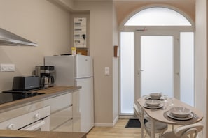 A modern kitchen with a stove, coffee maker, and refrigerator. There is a dining table with plates and a chair.