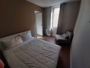 Une chambre d’hôtel avec un lit, une chaise, une fenêtre avec des rideaux et une porte.