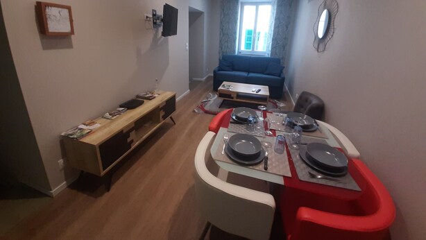 Un espace de vie compact comprenant un coin repas, un canapé et un téléviseur fixé au mur.