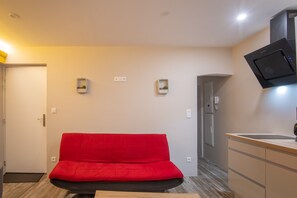 A room with a red sofa, a kitchen area, and a door leading to another room.