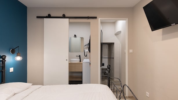 Une chambre à coucher comprenant un lit, une table de chevet, un téléviseur fixé au mur, et une salle de bain avec un lavabo et un miroir.