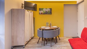 Un espace de vie compact comprenant un coin repas, un canapé rouge et un téléviseur fixé au mur.