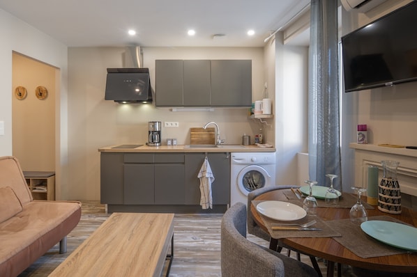 A compact kitchen with a washing machine, a coffee maker, and a flat-screen TV.