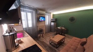 A living room with a sofa, a coffee table, a TV, a fireplace, a dining table, and a kitchen area with a microwave.