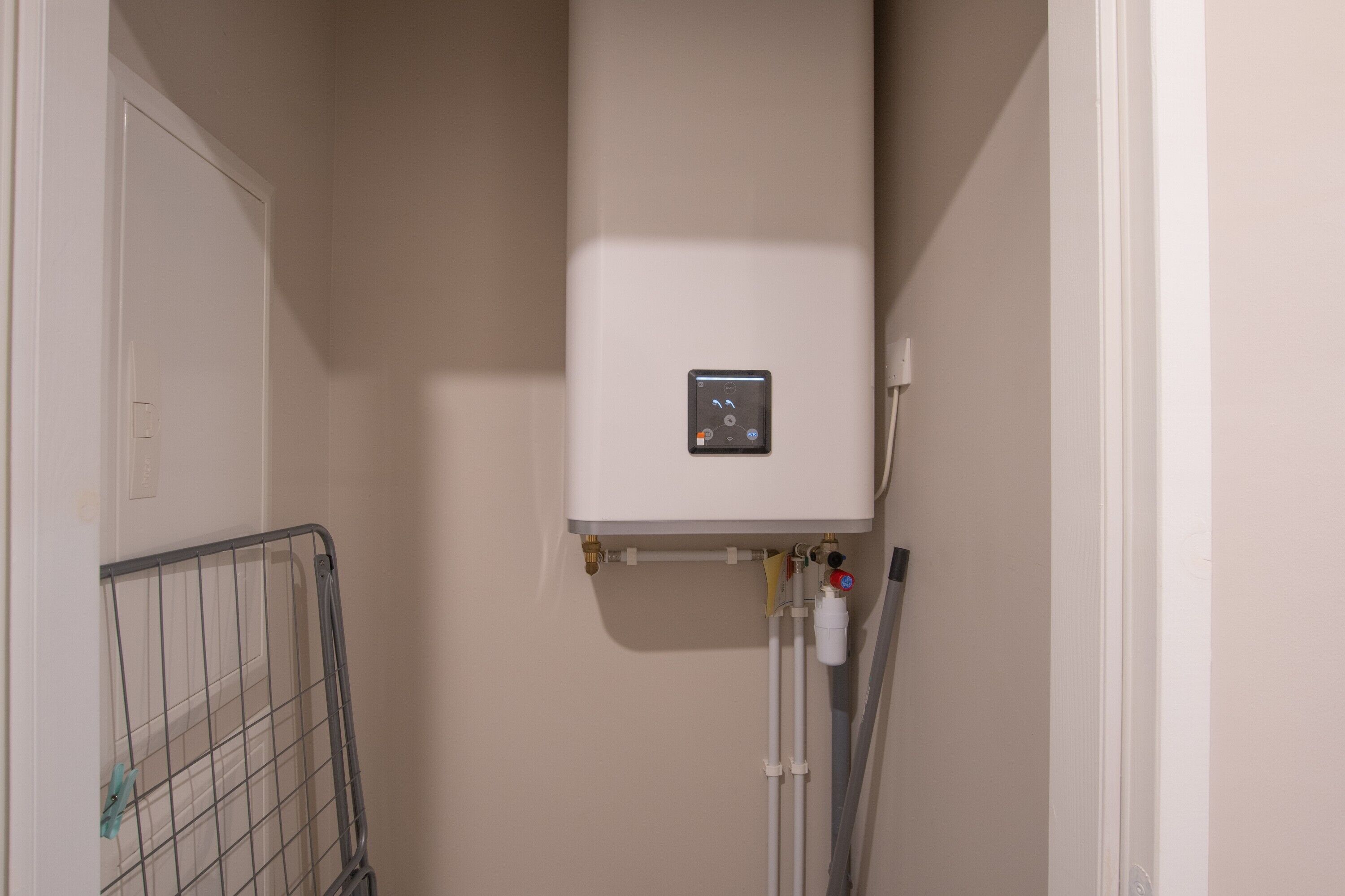 Ein weißer Boiler an einer Wand montiert, mit einer Steuerung, verbunden mit Rohren und Ventilen.
