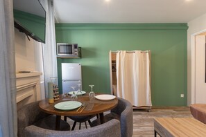 A dining area with a table set for two, a microwave, a refrigerator, and a shower curtain.