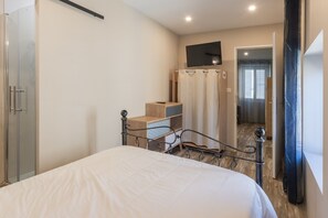 A bedroom with a bed, a wardrobe, a television, and a shower.