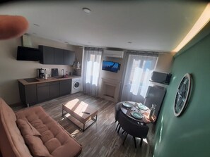 A compact living space with a sofa, dining table, kitchen area, and a TV.