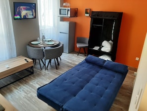 Une pièce comprenant un lit, une table à manger avec des chaises, un four à micro-ondes, un réfrigérateur et un téléviseur fixé au mur.