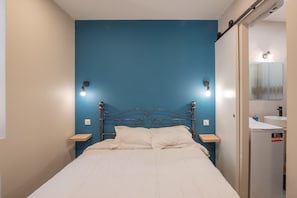 Une chambre à coucher comprenant un lit, des tables de chevet, un miroir fixé au mur et un lavabo intégré.