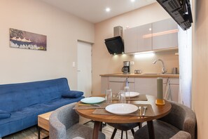 Un espace de vie compact comprenant une table à manger, des chaises, un canapé bleu, un coin cuisine avec un four à micro-ondes et un tableau accroché au mur.