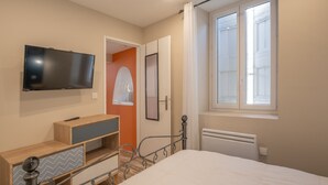 A bedroom with a bed, a TV mounted on the wall, a radiator, and a window with curtains.