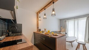 A modern kitchen with a wooden countertop, black tiles, and a breakfast setup. There is a dining area with a table and chairs.