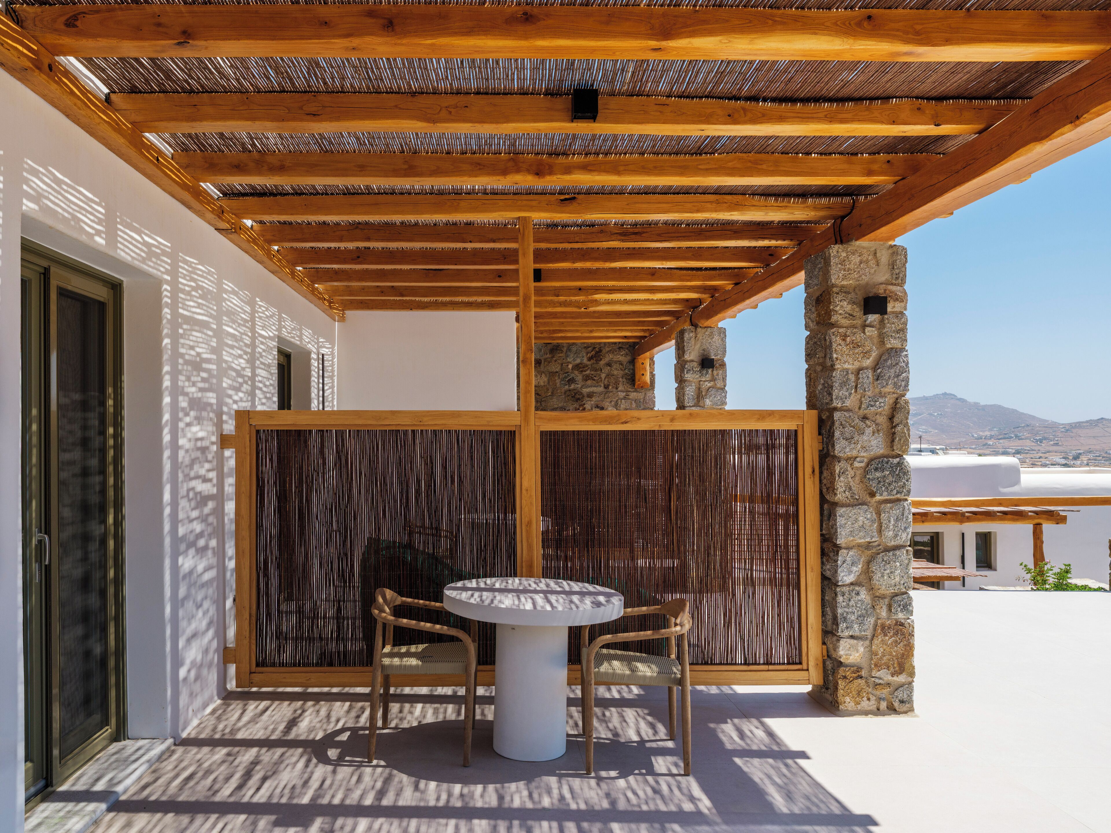 A covered outdoor seating area with a table and chairs, stone pillars, and a view of the landscape.