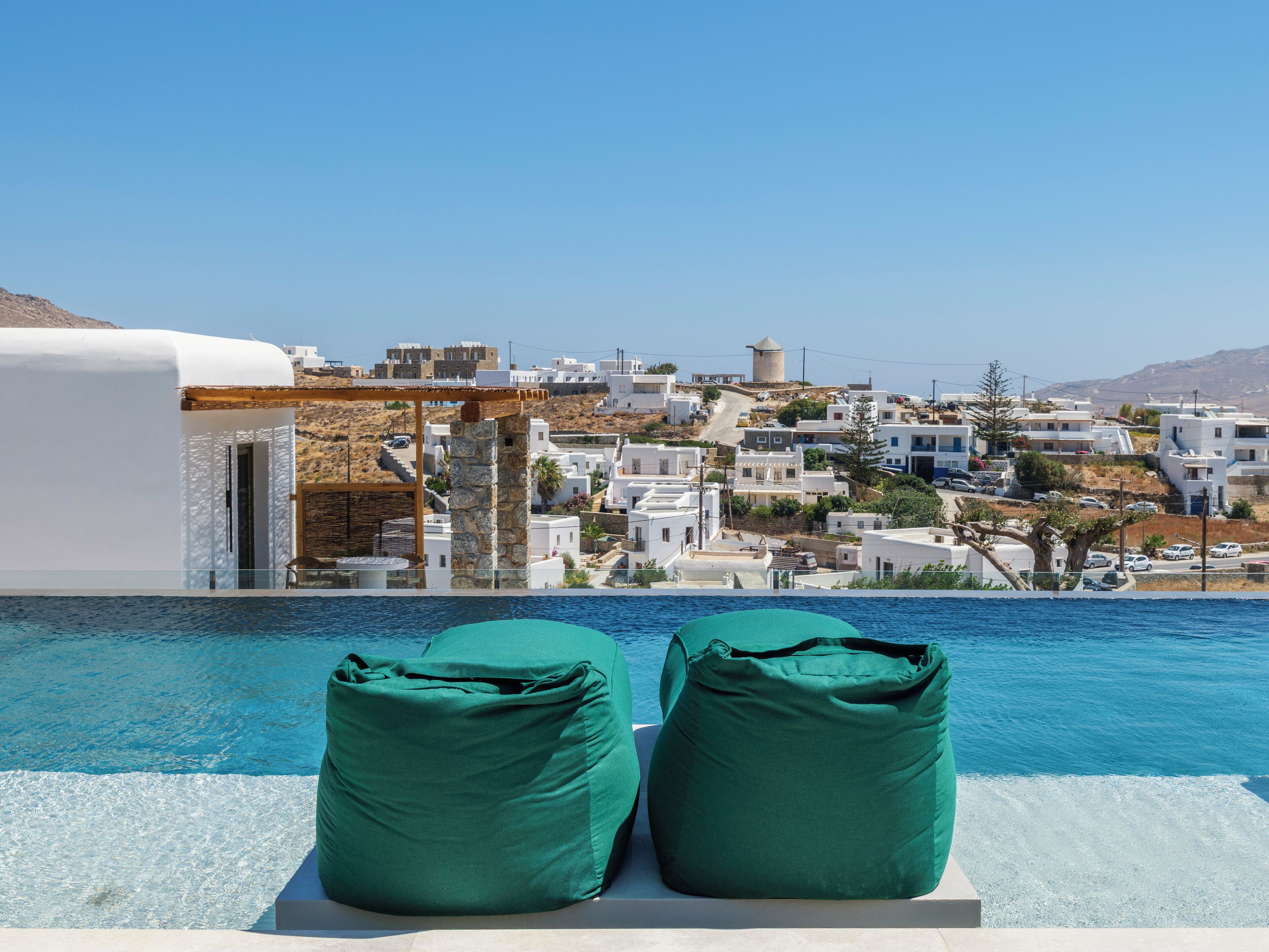 A poolside view with two green lounge chairs, a clear blue sky, and a coastal town in the background.
