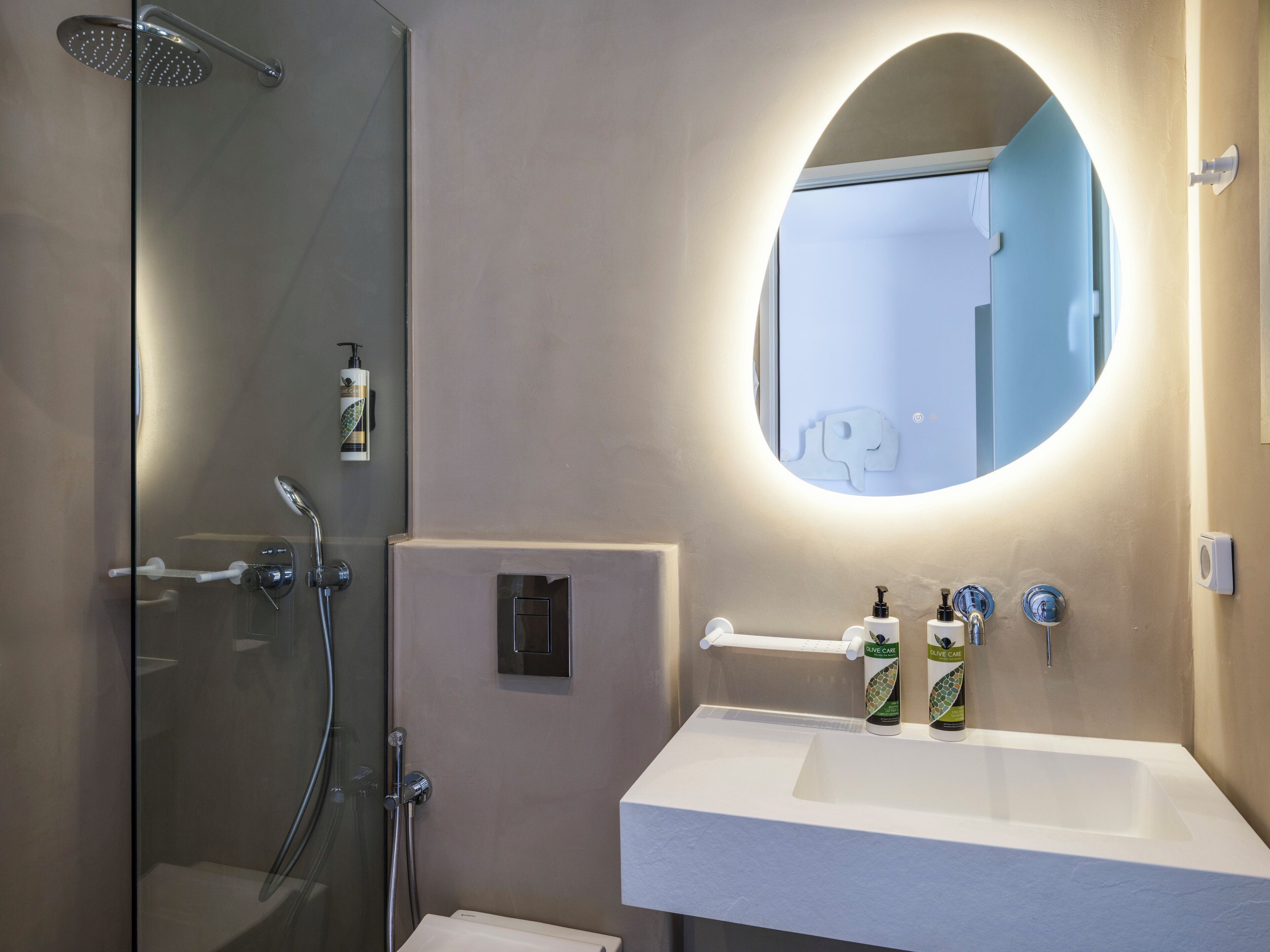 A modern bathroom with a glass shower enclosure, a white sink with a mirror above it, and toiletries on the sink.