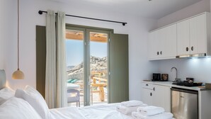 A hotel room with a bed, a kitchenette, and a sliding glass door leading to an outdoor area. - Mykonian Shades (Ano Mera)