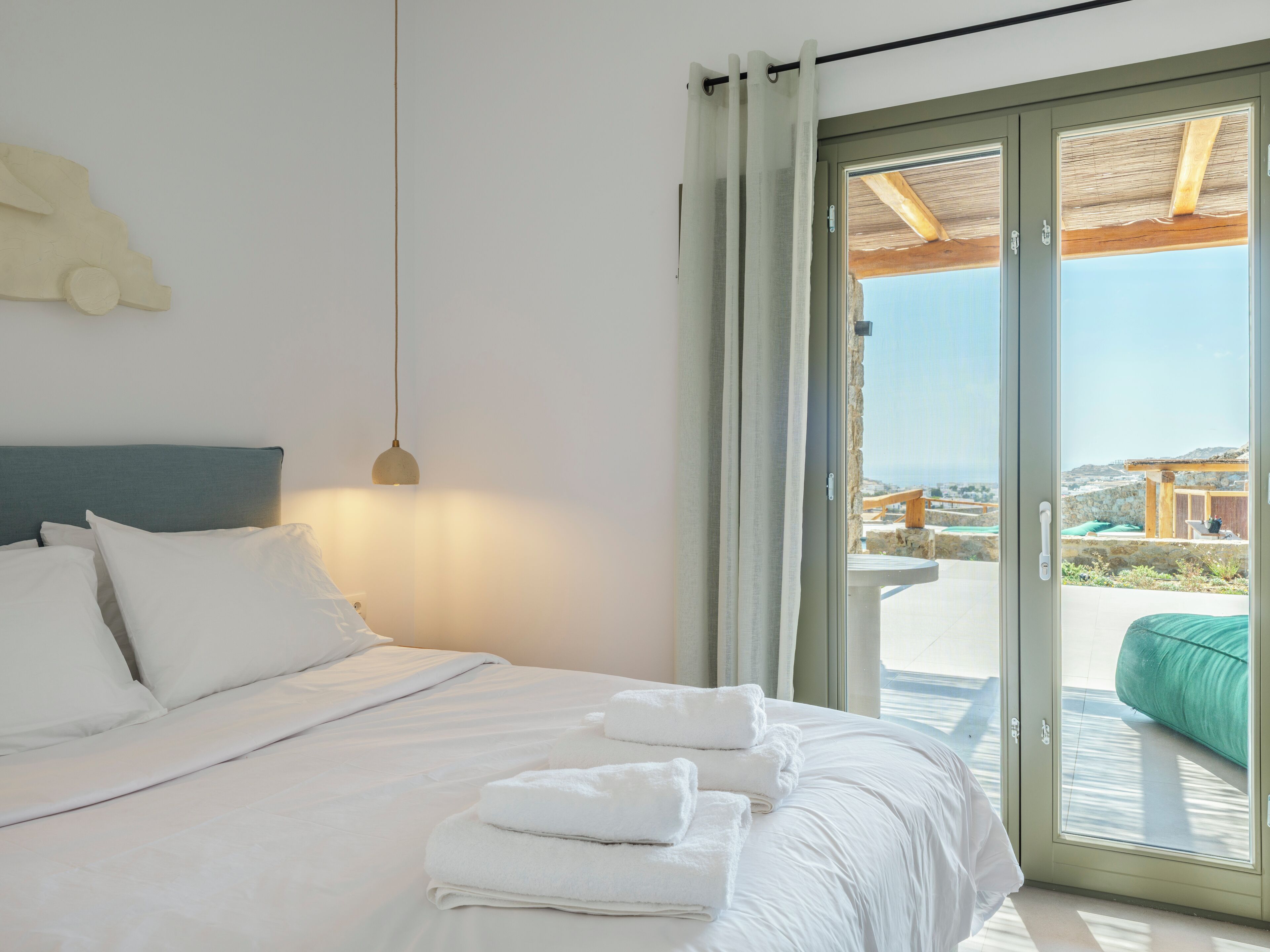 A bedroom with a bed, white pillows, a bedside lamp, and a view of the outdoors through a sliding door.