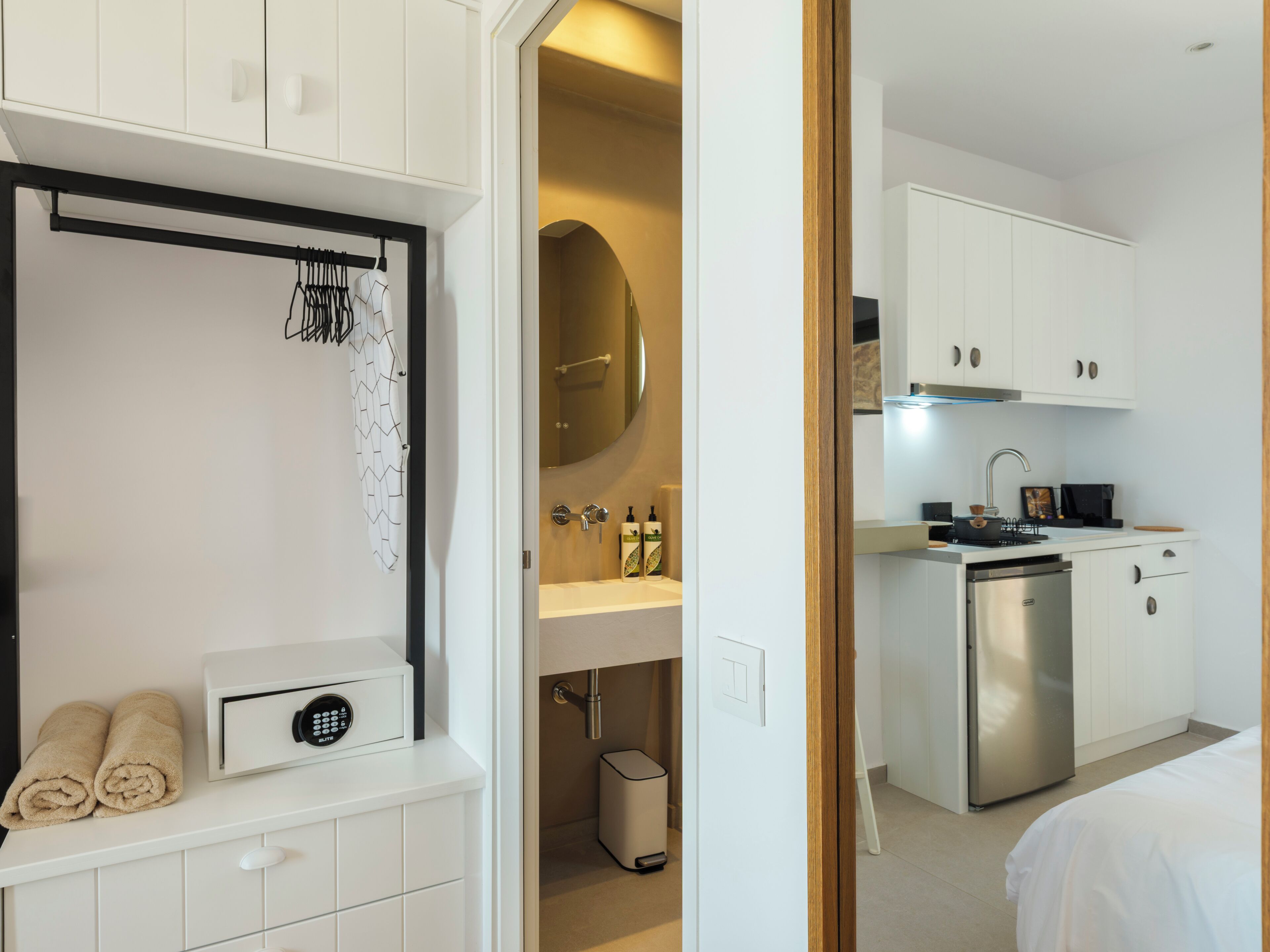 Una habitación de hotel moderna con vestidor, baño con lavabo y espejo, y kitchenette con lavavajillas.