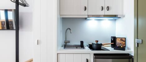 A compact kitchen with white cabinets, a stainless steel refrigerator, a sink, and a small countertop with a kettle and a coffee machine.