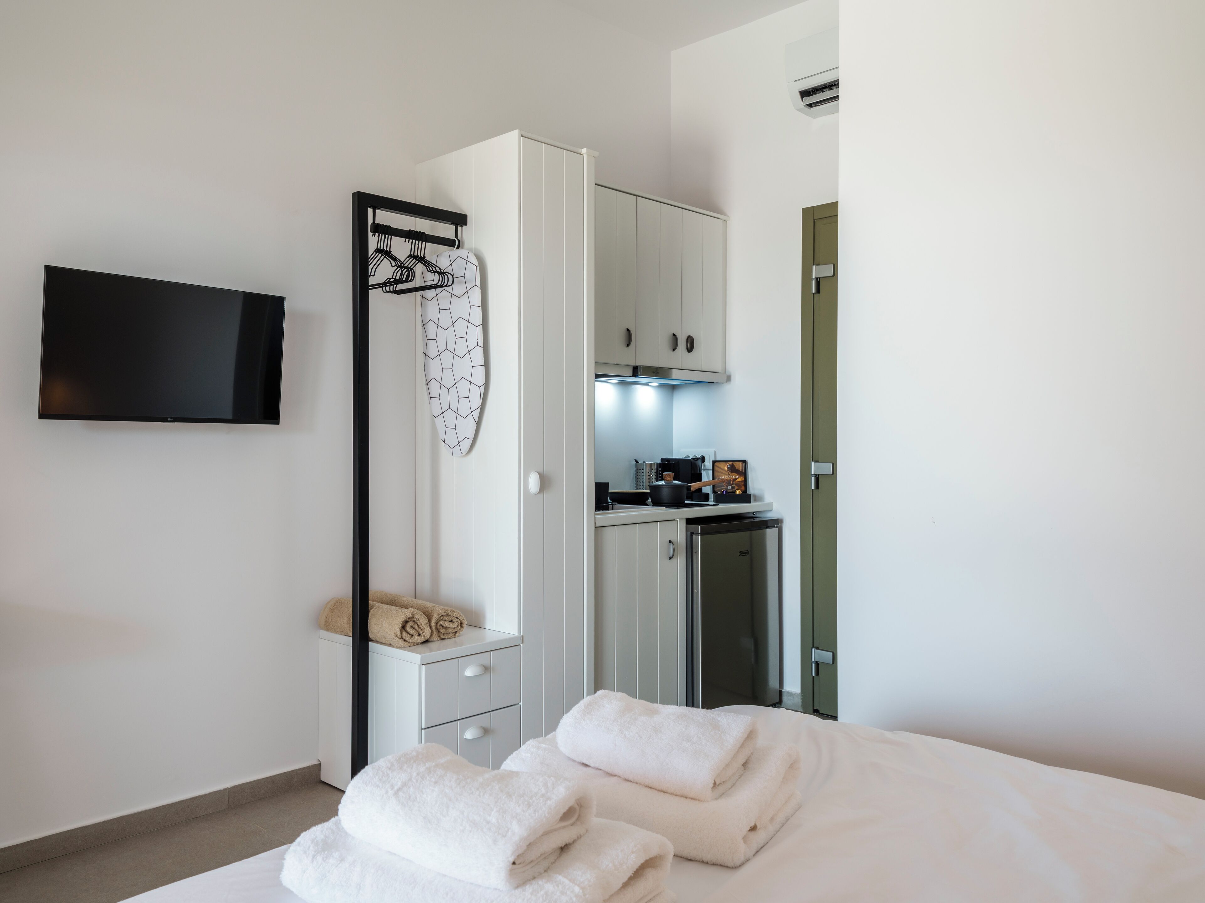 Una camera d'albergo moderna con un letto, una TV a parete, un armadio, un angolo cottura e un bagno.