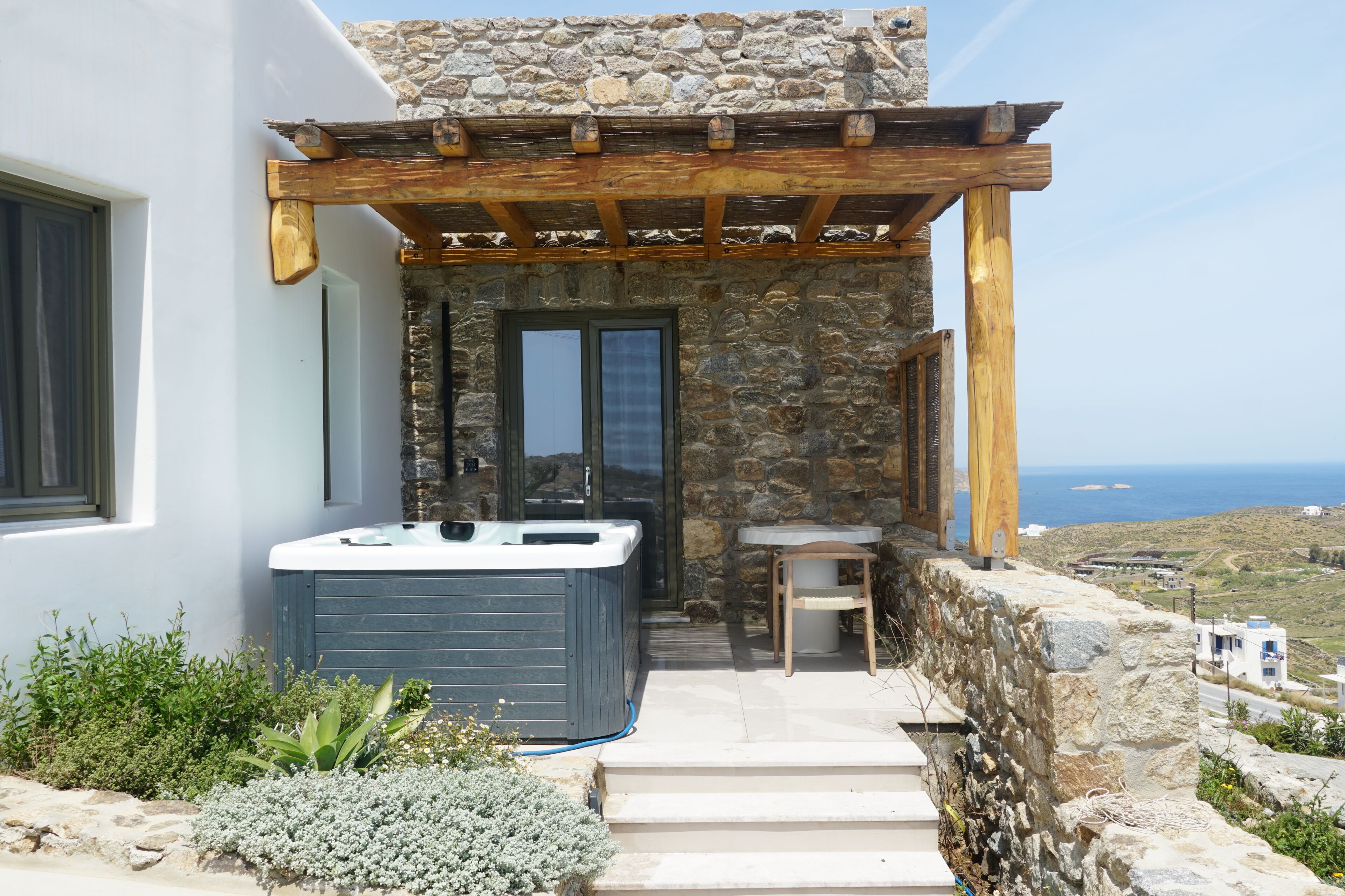 A stone building with a hot tub, a wooden pergola, and a view of the sea.