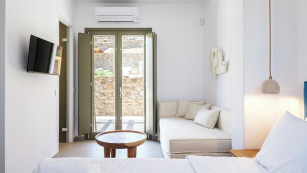 Un dormitorio moderno con una cama, un sofá, una mesita y un televisor en la pared.