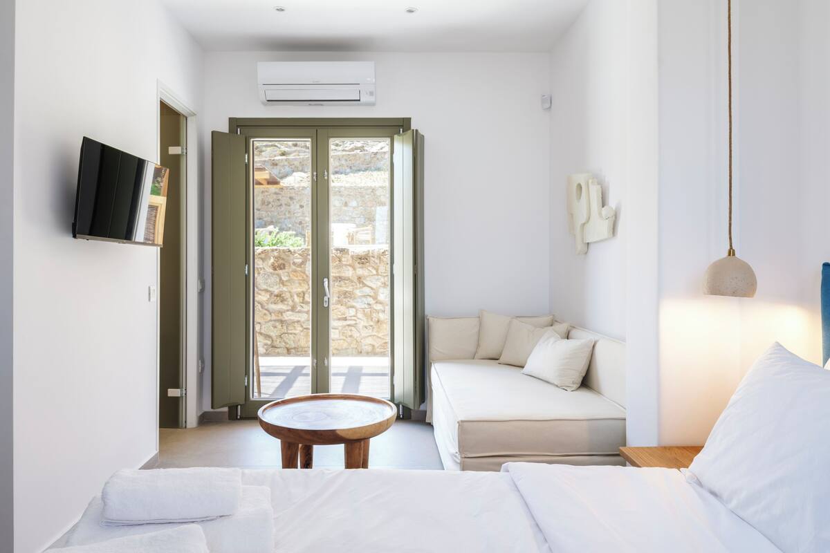 Un dormitorio moderno con una cama, un sofá, una mesita y un televisor en la pared.