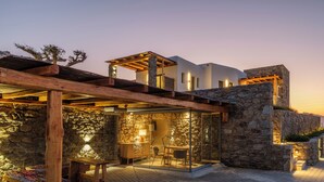 A stone building with a wooden pergola and a glass enclosure, featuring a table and chairs. - Mykonian Shades (Ano Mera)