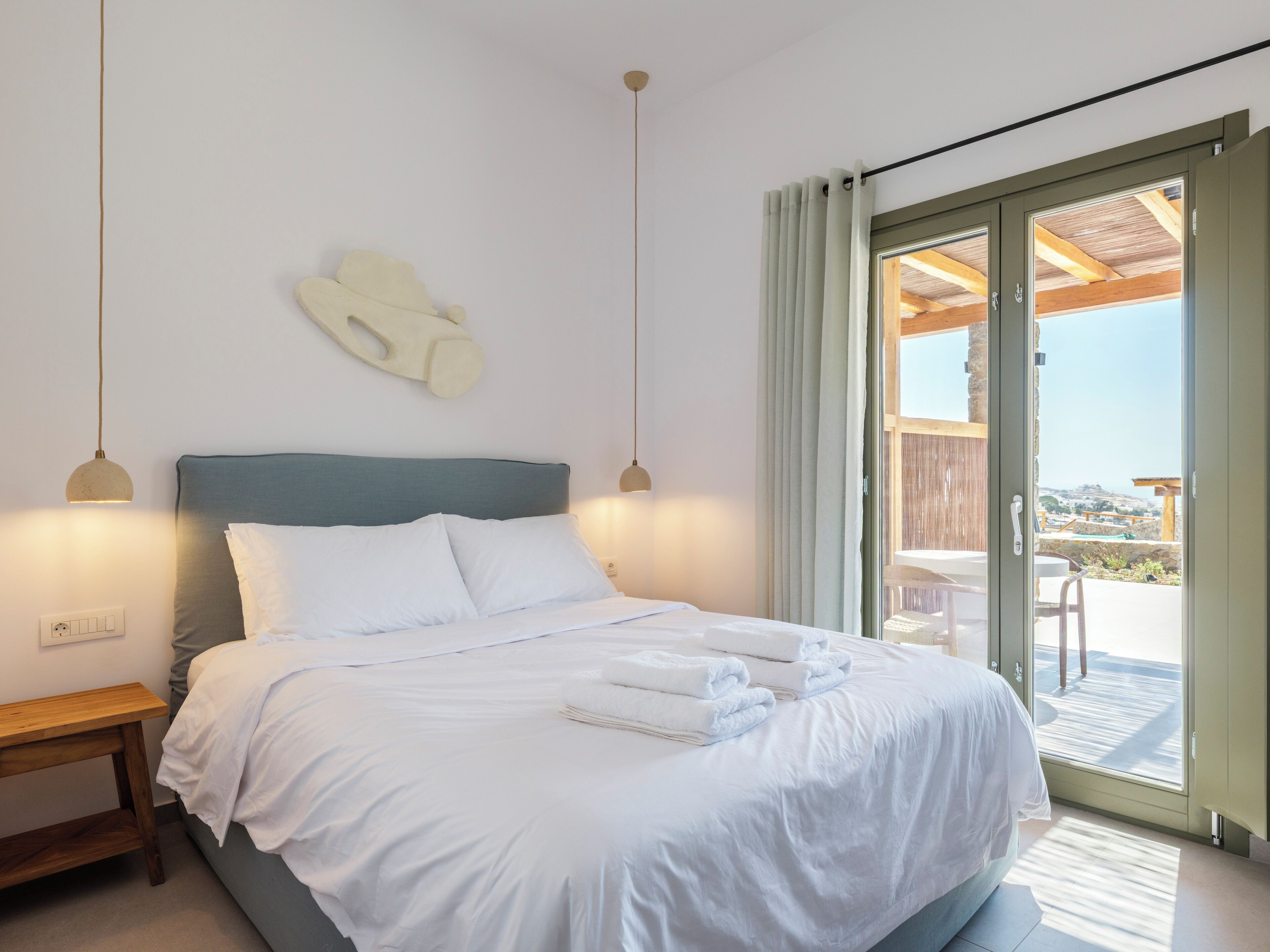 A bedroom with a bed, bedside tables, a wall-mounted light fixture, and a sliding glass door leading to an outdoor area.
