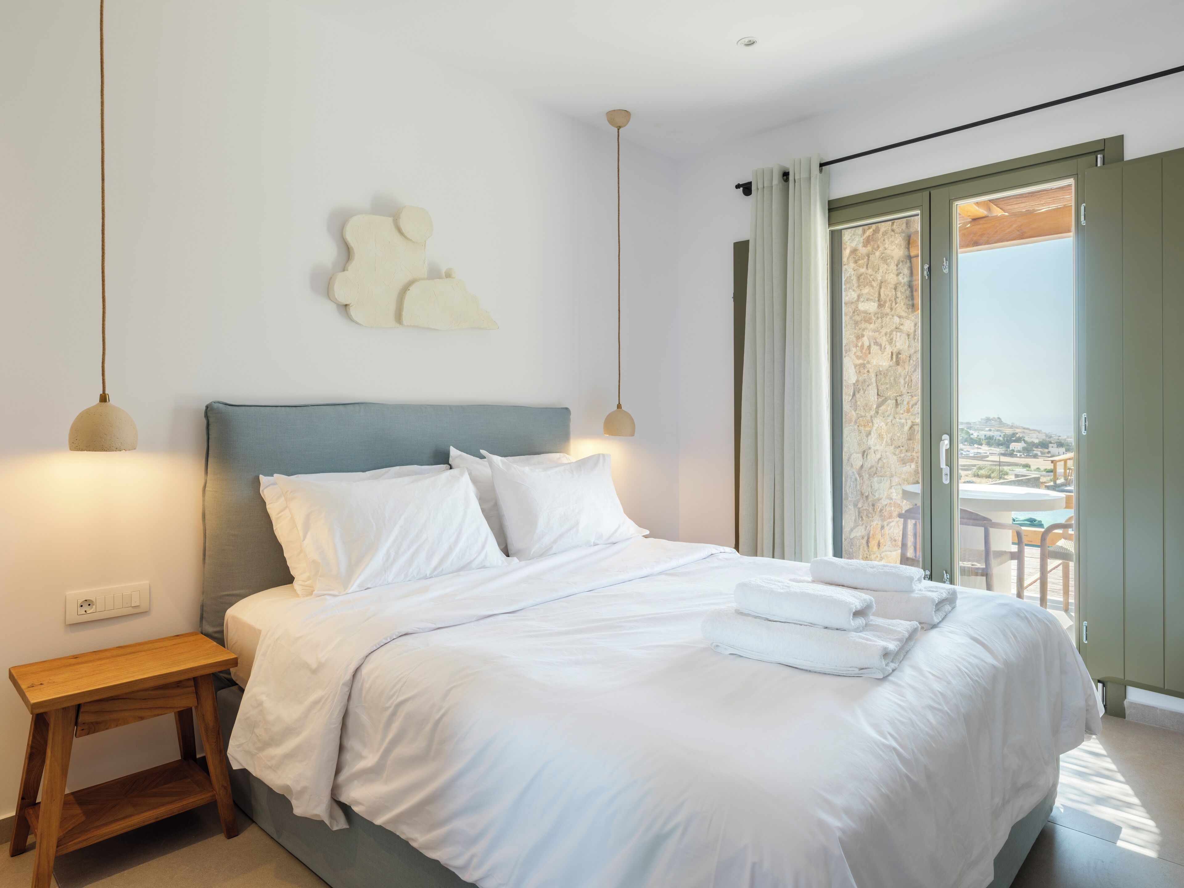 A bedroom with a bed, bedside table, and a view of the outside.
