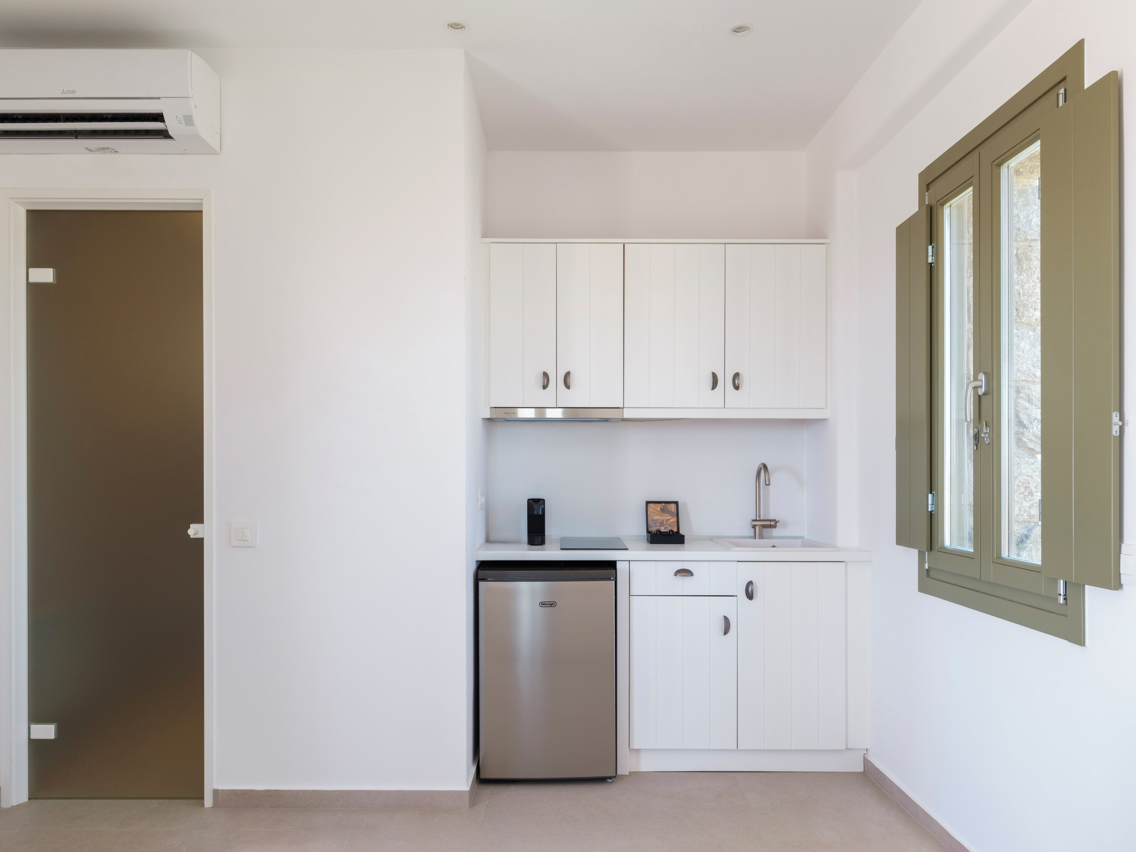 A compact kitchen with white cabinets, a stainless steel dishwasher, and a window with a green frame.