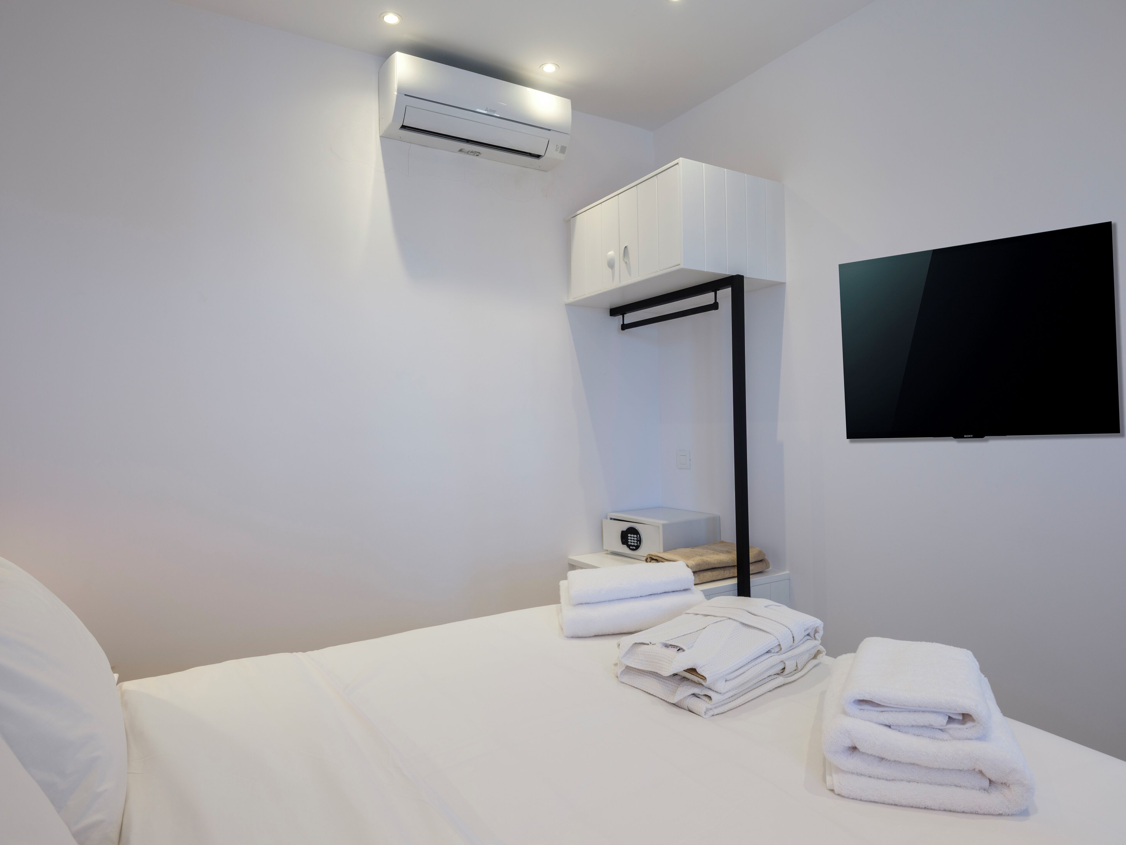 A hotel room with a bed, a TV mounted on the wall, an air conditioning unit, and a small table with towels.