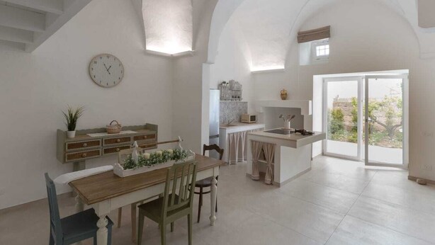 Une cuisine spacieuse avec un coin repas, une horloge au mur et une vue à travers la porte vitrée.
