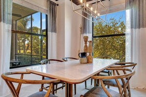 A dining area with a marble table and wooden chairs, large windows, and a modern chandelier.
