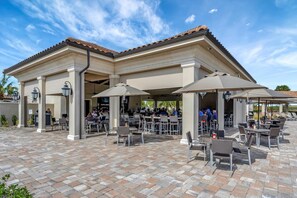 An outdoor patio with tables and chairs, a covered seating area, and a building with a tiled roof. - Play Golf & Pickleball! Luxury Lakewood Townhome (Bradenton)
