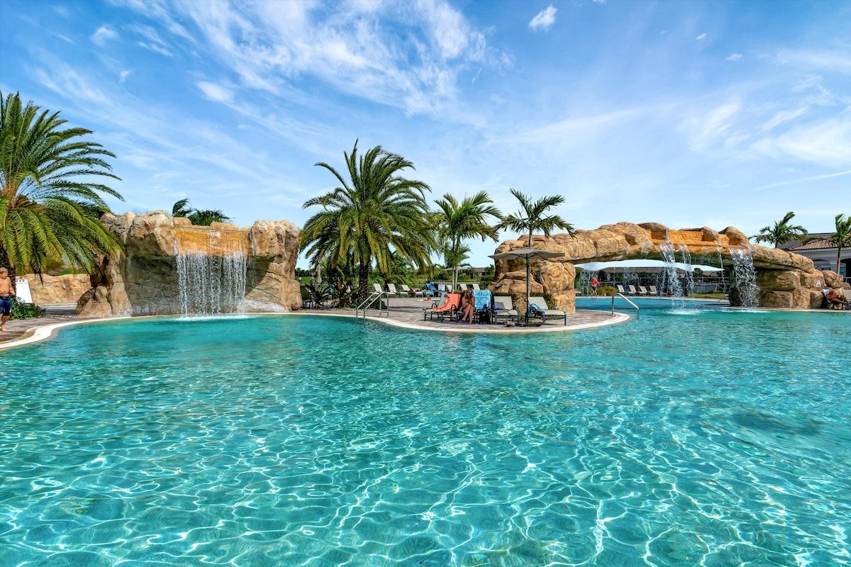 A clear blue pool with palm trees and rock formations.