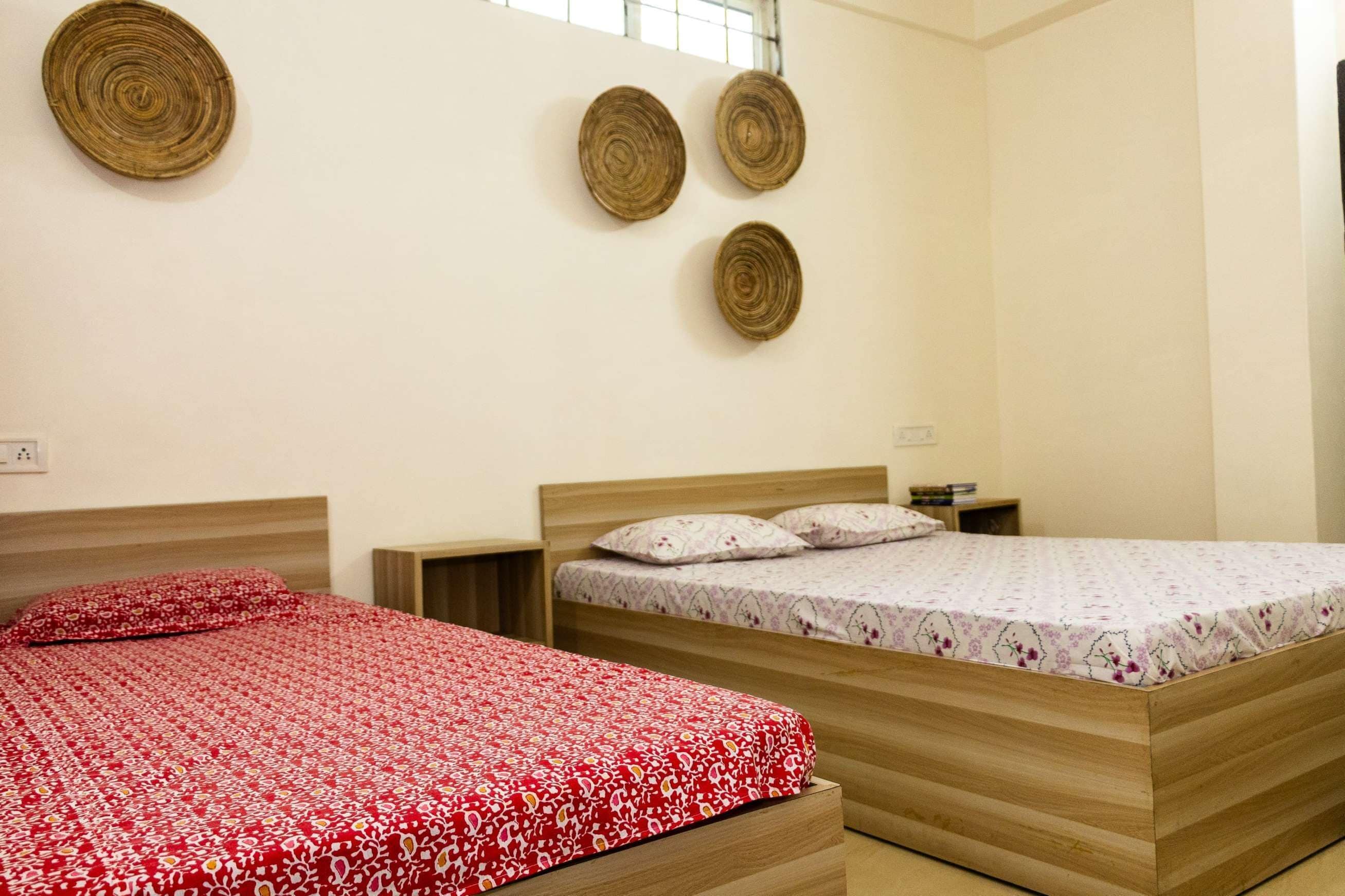 Una habitación con dos camas de madera, cada una con una colcha de estampado floral. Hay tres adornos de pared tejidos y una mesita de noche con un libro.