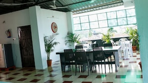 A dining area with a checkered floor, a table with chairs, potted plants, and a window with a view. - Malini Homes - Food & Lodging (Guwahati)