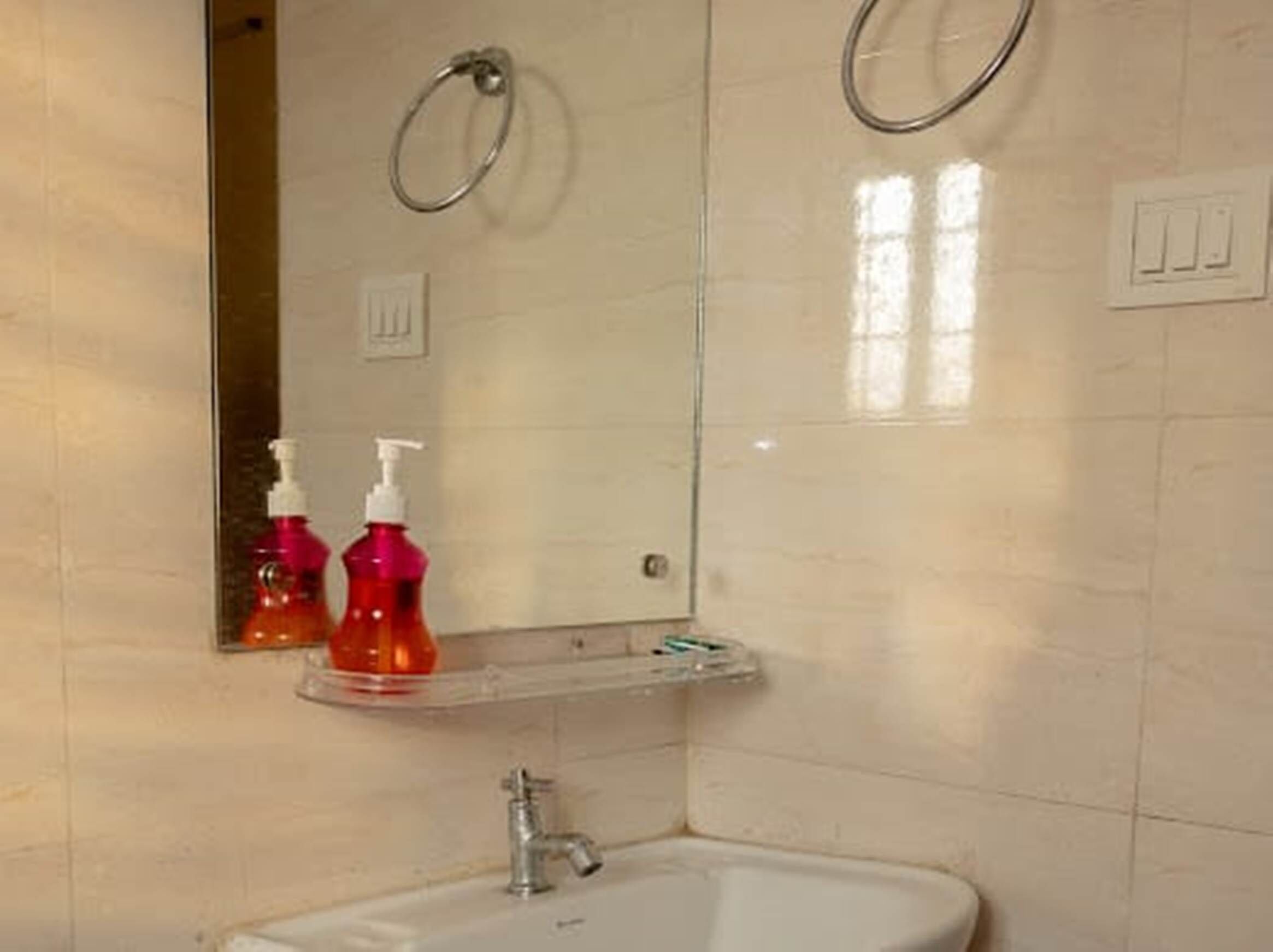 Une salle de bain équipée d’un lavabo, de deux distributeurs de savon liquide, d’un miroir et d’un porte-serviette.