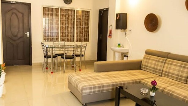 A living room with a sofa, a coffee table, a dining table with chairs, and a window with blinds. - Malini Homes - Food & Lodging (Guwahati)