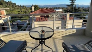 Un balcone con un tavolino in vetro e due sedie in vimini, con vista su un paesaggio collinare con edifici e cielo sereno.