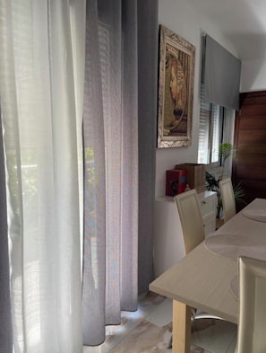 A dining area with a table, chairs, a painting on the wall, and a window with curtains. - Terrific building with AC in charming Eretria, Greece (Ερέτρια)