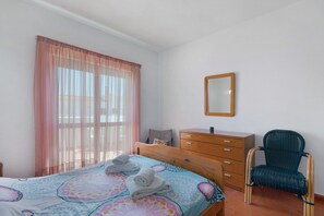 Une chambre à coucher avec un lit, une commode en bois, une chaise et un miroir au mur.