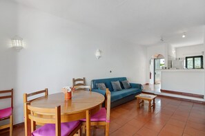 Un salon avec une table ronde en bois, un canapé bleu et, au fond, un coin cuisine.