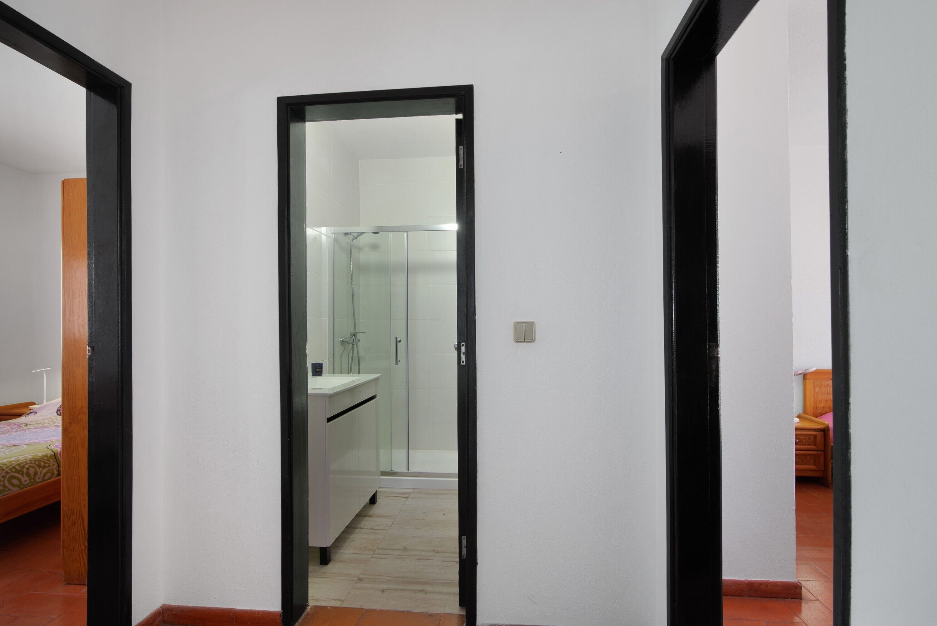 Un couloir étroit, avec une porte miroir donnant sur une salle de bain dotée d’une douche à parois de verre.